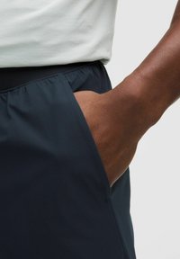 Pantalones cortos de color marino con una textura suave, cinturilla elástica y un bolsillo lateral. Una mano está colocada dentro del bolsillo, destacando el diseño.