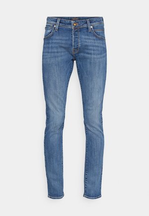 Kitsas sinised denim püksid, millel on kerge pleekimine, klassikaline viie tasku disain, kollased õmblused ja metallist detailid taljes.