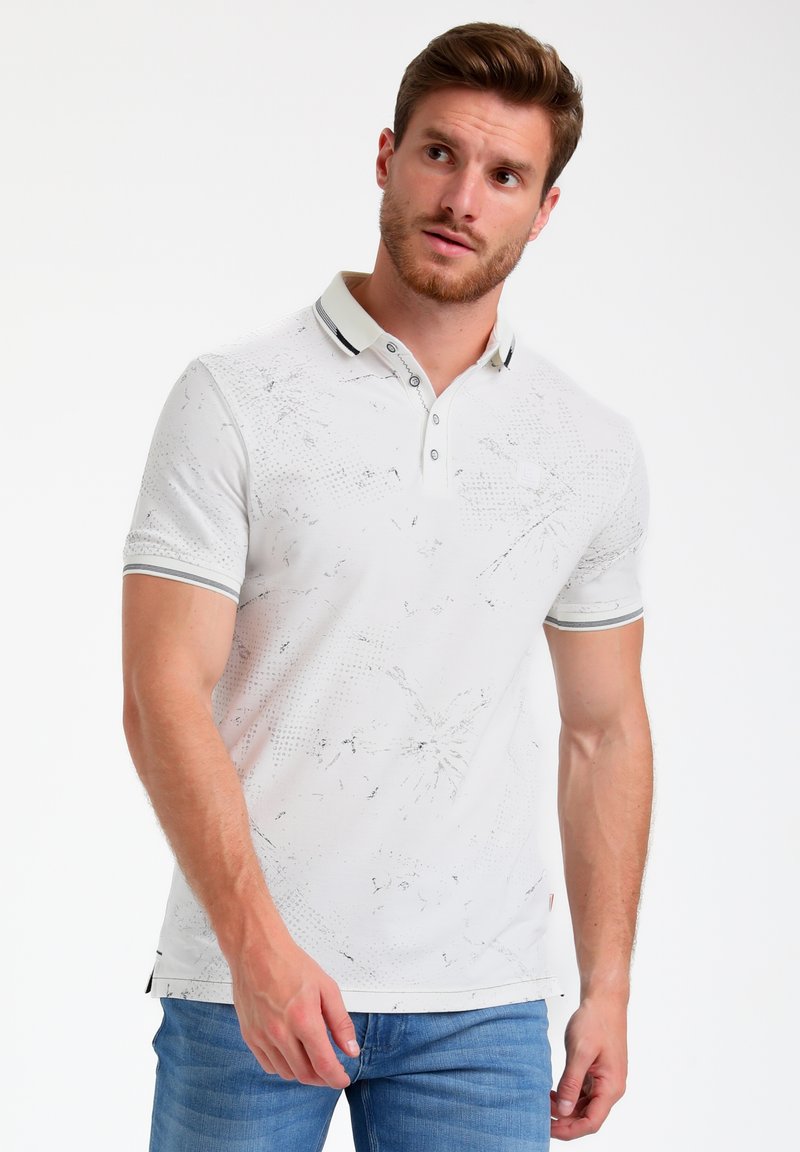 Polo bianco con un motivo testurizzato, colletto con due bottoni e dettagli neri, abbinato a jeans azzurri chiari.