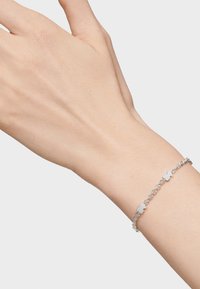 Pulsera delicada de cadena de plata con pequeños charms en forma de flor en la muñeca de una persona contra un fondo claro.