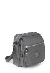 Graue Crossbody-Tasche aus Stoff mit mehreren Reißverschlussfächern, rundem Logo-Detail und einem dekorativen Anhänger am Reißverschluss.