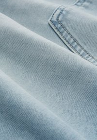 Tela de mezclilla de color azul claro con una textura suave, que presenta desvanecimientos sutiles y costuras ordenadas. Primer plano de la trama del material y variaciones de color.