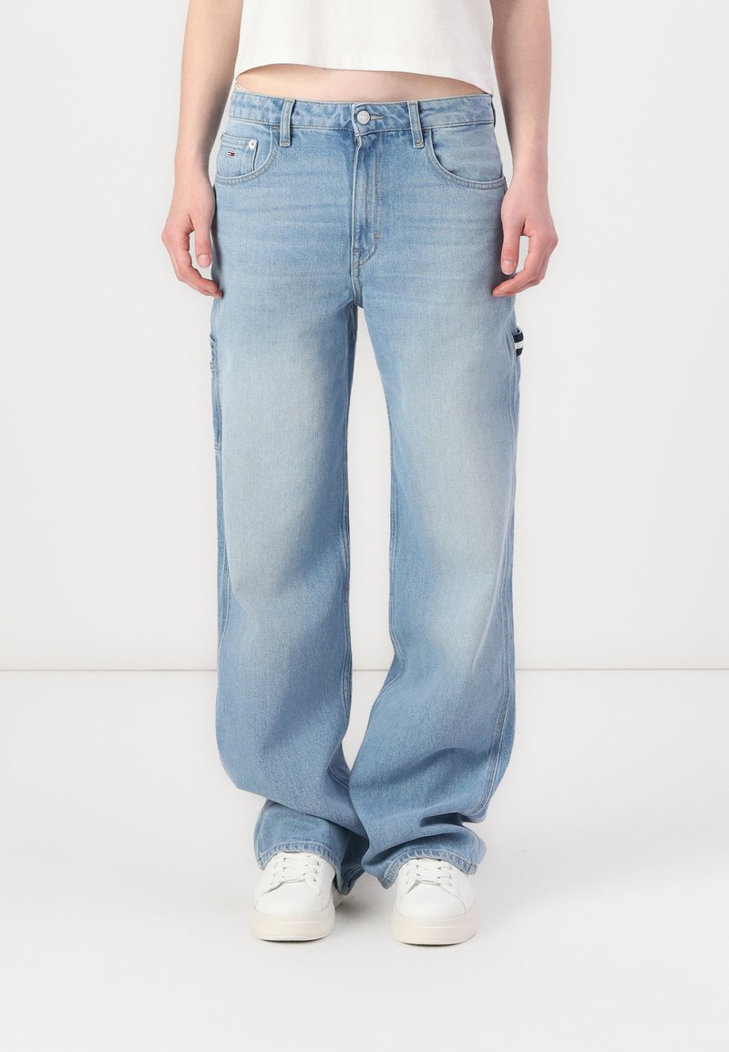 Lichtblauwe wijde jeans met een hoge taille, voorzakken en zij cargos. Gemaakt van denim met een vervaagde afwerking. Witte sneakers gedragen.