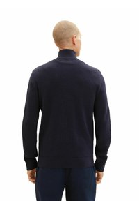 Pull en maille bleu marine à col haut et texture côtelée. Présente des manches longues et un ourlet ajusté, conçu pour un ajustement près du corps.