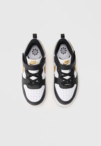 Nike sportbačiai su juodos ir baltos odos apdaila, auksiniais akcentais, tinklinėmis pamušalo detalėmis, perforuota pirštų dėžute ir Velcro juosta.
