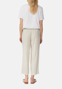 T-shirt en coton blanc associé à un pantalon ample beige clair et des sandales plates. Le pantalon a une taille élastique et des jambes larges.