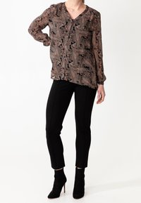 Långärmad blus i svart med paisleymönster, med knappar och V-ringning, matchad med figurnära svarta byxor och ankelboots.