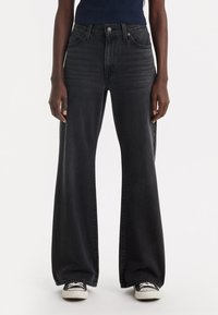 Jean noir taille haute avec un design à jambes larges, fabriqué en denim, doté de poches avant, d'une fermeture à bouton et de détails de décoloration subtils.