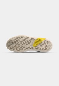 Semelle de chaussure avec des motifs circulaires, un dessin rond type cible près du talon, et une mise en évidence jaune sur la zone de la voûte plantaire sur fond blanc.