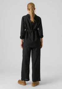 Czarny lniany zestaw składający się z bluzki z długim rękawem i paskiem oraz spodni o szerokich nogawkach. Do wyróżniających się detali należą podwinięte rękawy i miękka tekstura.