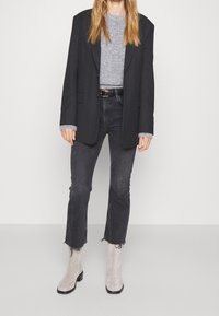 Blazer negro sobre un suéter de punto gris, combinado con jeans oscuros deshilachados y botines de ante gris claro con tacón bajo.