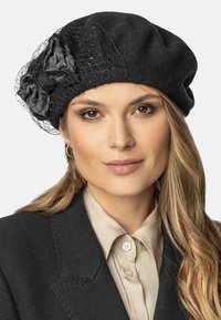 Beret en laine noire avec un filet et des accents de fleurs en soie, présentant une forme ronde et une surface texturée. Conçu pour un look ajusté.