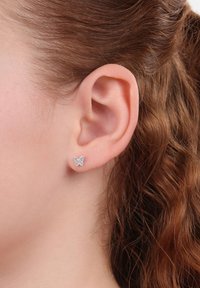 Orecchini a perno a forma di farfalla in argento, decorati con gemme trasparenti, presentati in un design delicato, indossati da una persona con capelli ricci e castani.