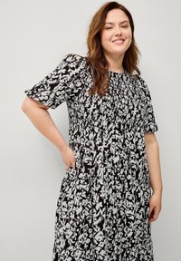 Schwarz-weißer Blumenkleid mit kurzen Puffärmeln, gerafftem Oberteil und fließendem Rock; verfügt über eine geraffte Textur und Seitentaschen.