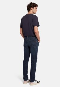 Jeans en denim bleu foncé avec une coupe droite, présentant un design traditionnel à cinq poches et de subtils motifs de couture sur les poches arrière.