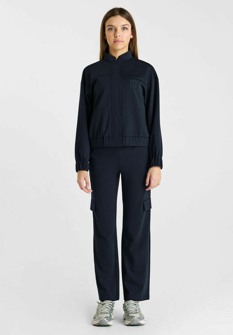 Zwarte sportieve trainingspak met een ritsjack met elastische manchetten en broeken met cargozakken, gemaakt van gladde, rekbare stof.