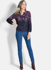 Bloes met bloemmotief in donkere tinten met paarse accenten, lange poffende mouwen en een v-hals. Gecombineerd met strakke blauwe jeans en hoge hakken.