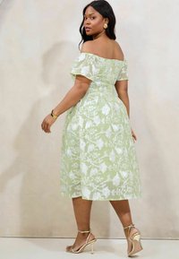 Rochie verde deschis, cu umerii la vedere, cu broderie florală albă, siluetă în formă de A, până la genunchi, asociată cu sandale aurii cu bretele.