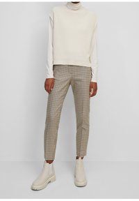 Haut sans manches crème côtelé associé à un pantalon à carreaux marron et blanc. Bottines beiges avec semelles épaisses et panneaux élastiques latéraux.