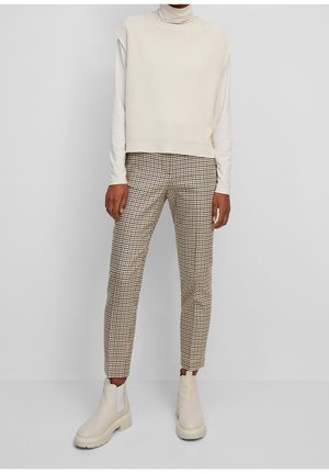 Haut sans manches crème côtelé associé à un pantalon à carreaux marron et blanc. Bottines beiges avec semelles épaisses et panneaux élastiques latéraux.