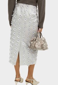 Falda midi blanca con apliques florales y una abertura en la parte trasera, combinada con un bolso de piel de serpiente y zapatos de tacón de color claro.