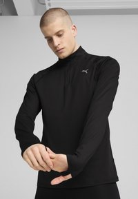 Zwarte atletische top met lange mouwen en een ritssluiting bij de kraag, met een gladde textuur en reflecterend logo detail op de borst, ontworpen voor prestaties.