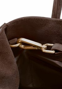 Wnętrze brązowej torby z zamszu z metalowym złotym zaciskiem i okuciami. Miękka faktura, solidna konstrukcja i funkcjonalne zamknięcia kontrastujące z gładką podszewką.