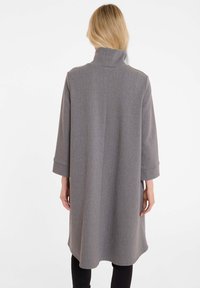 Grauer übergroßer Mantel mit hohem Kragen, Dreiviertelärmeln und subtiler Nadelstreifenstruktur, der bis zur Mitte des Oberschenkels reicht.