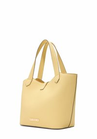 Gul texturerad tote bag med två axelremmar, med en minimalistisk design och ett metallmärke på framsidan.