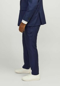 Costume marine avec une coupe ajustée, fabriqué en tissu lisse. Assorti à des baskets blanches, montrant une texture subtile et un look contemporain.