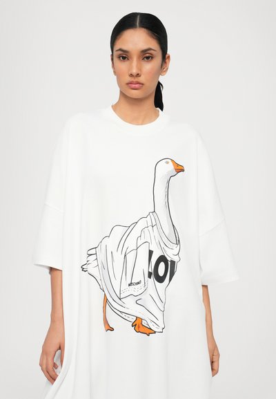 T-shirt oversize blanc présentant une illustration d'une oie portant un maillot, avec des accents noirs et oranges. Texture de tissu lisse.