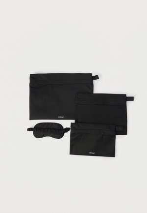 Tri crne torbice s patentnim zatvaračem različitih veličina i crna maska za spavanje s elastičnom trakom, sve položeno na bijelu površinu.