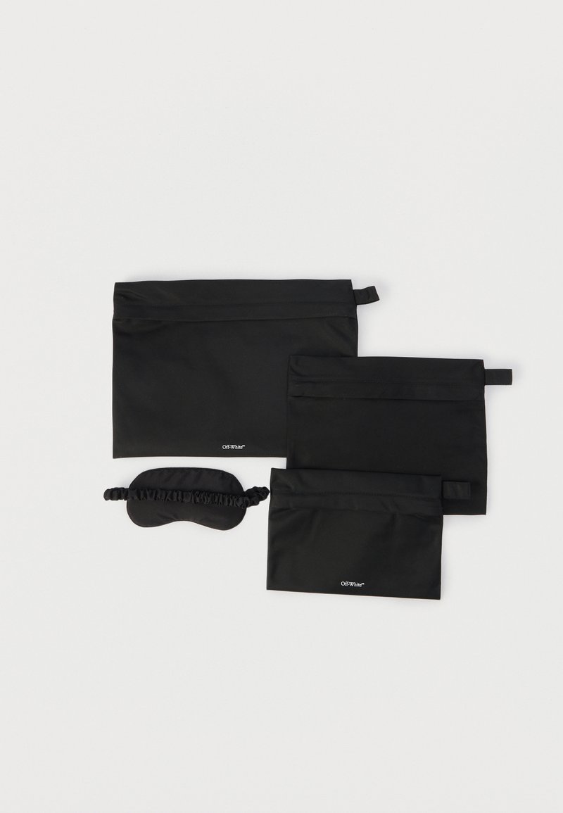 Τρεις μαύρες θήκες με φερμουάρ σε διάφορα μεγέθη και μια μαύρη μάσκα ύπνου με ελαστικό λουράκι, όλα τοποθετημένα σε λευκή επιφάνεια.