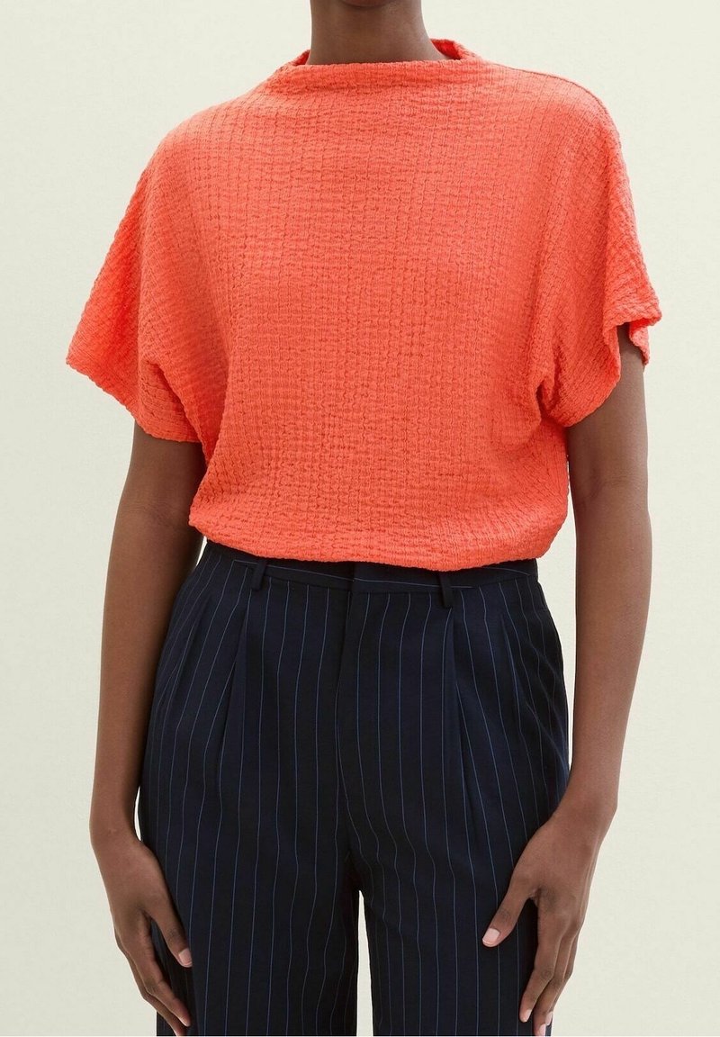 Top corto a maniche corte arancione con texture e scollatura rotonda, abbinato a pantaloni blu scuro con righe sottili. Design casual e dal taglio morbido.