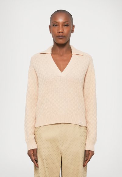 Pull en tricot rose clair avec un col en V, texture à motifs et un col. Ourlets et manches côtelés. Assorti à un pantalon beige à pois.