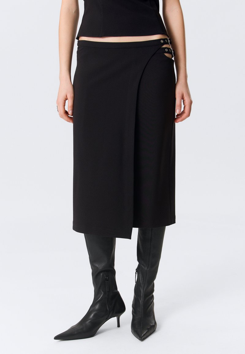 Μαύρη ζώνη μέσης μεσαίου μήκους με πλευρική αποκοπή και διπλή αγκράφα, συνδυασμένη με μαύρες μπότες έως το γόνατο με μυτερή μύτη.