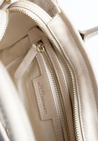 Beige leren tasinterieur met een gladde textuur, gouden rits en een klein zijvak met een mer etikette.