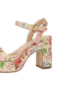 Escarpin à motif floral avec un talon épais, fabriqué en tissu texturé de couleur crème, doté d'une bride ajustable à la cheville et d'une boucle dorée.