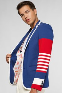 Blauwe blazer met een rood gestreepte mouw. Witte afwerking en knopen. Gevoerd met een speels patroon van hotdogs en frietjes. Getailleerde fit.