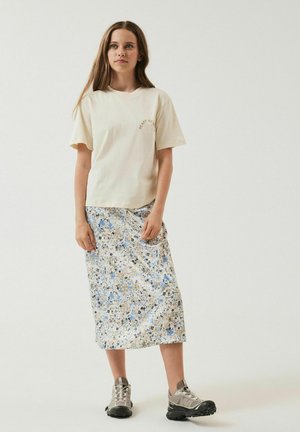 T-shirt crema a maniche corte con il testo "Peace of Mind", abbinato a una gonna midi a fantasia floreale blu e beige, completato da sneakers grigie.