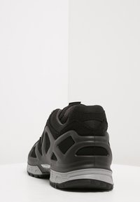 Schwarzer Sportschuh mit strukturiertem Obermaterial, geschwungenem Design, verstärktem Fersenbereich und grauen Akzenten an der Zwischensohle und der Außensohle.