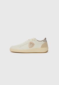 Low-top cream sneaker with beige sole, embroidered shield logo on side, snake-patterned trim at heel, and lace-up closure.