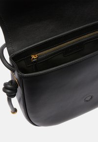 Borsa a mano in pelle nera con finitura liscia, dotata di una tasca interna con zip dorata e un dettaglio in pelle annodato sulla tracolla.