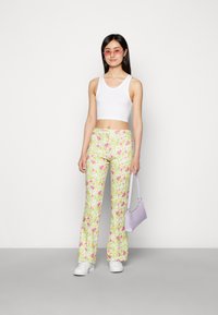 Calças de boca de sino estampadas com flores em verde claro com flores rosas, combinadas com um top curto branco e uma mala lavanda. Calçado: ténis brancos.