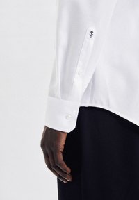 Witte shirt met een gestructureerde kraag, knopenmanchetten en geborduurde bloemen op de mouw. De stof heeft een gladde textuur.