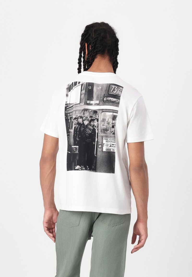 Hvid bomulds T-shirt med et stort sort-hvidt fotografisk print af mennesker ved en busstop på ryggen. Rund halsudskæring, afslappet pasform.