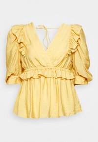 Blouse en satin jaune avec manches bouffantes, encolure en V profonde, bordure à volants à la taille et aux épaules, et fermeture par lien à l'arrière du col.