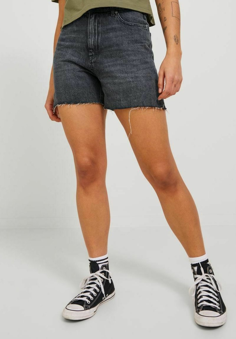 Shorts de mezclilla negra con dobladillo deshilachado, diseño de cintura alta, combinados con zapatillas altas negras. Tela texturizada lisa, estilo casual.
