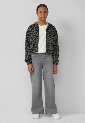 Gekürzte Jacke mit schwarzem und grauem Leopardenmuster, aus gestricktem Material, mit elastischen Bündchen; kombiniert mit grauen weiten Jeans und weißen Sneakern.