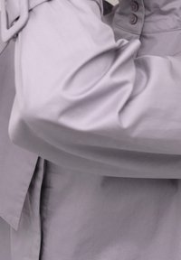 Jasnoszara koszula z miękkiego materiału o luźnym kroju, z detalami w postaci guzików i unikalnym kształtem rękawów.